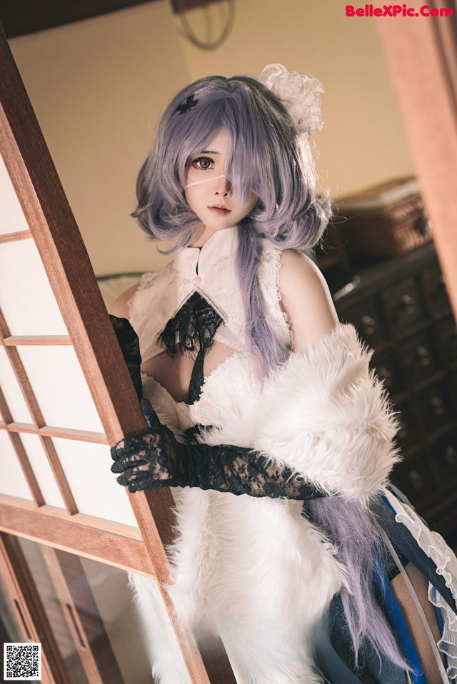 A woman with purple hair wearing a white fur coat.