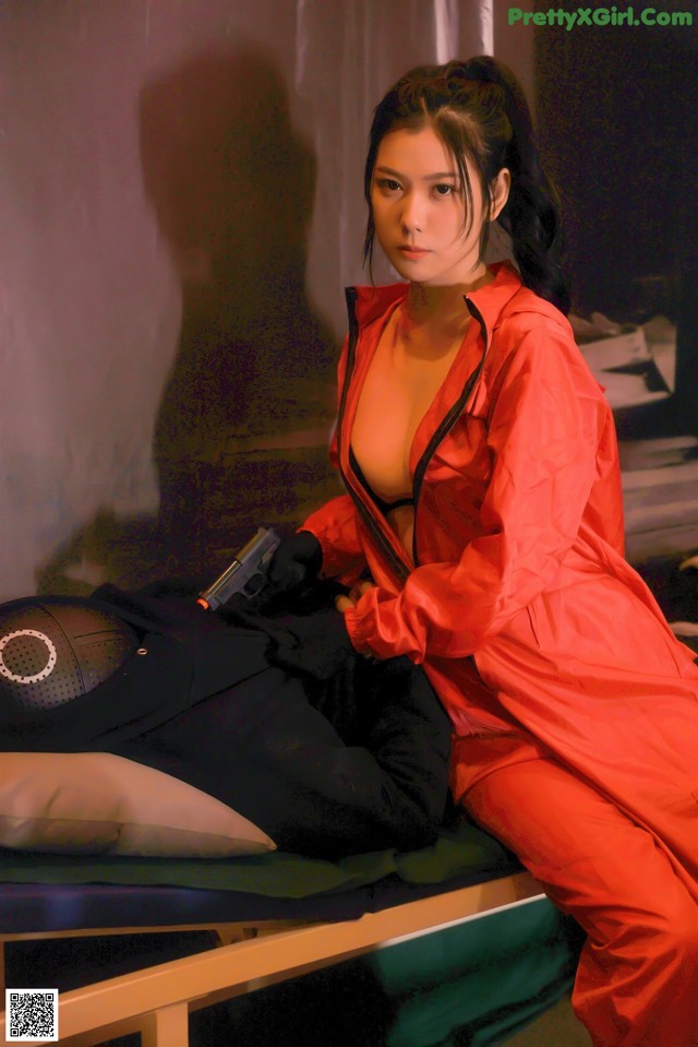 A woman in a red jumpsuit sitting on a bed.