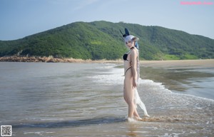 A woman in a bikini sitting on a beach next to a painting.