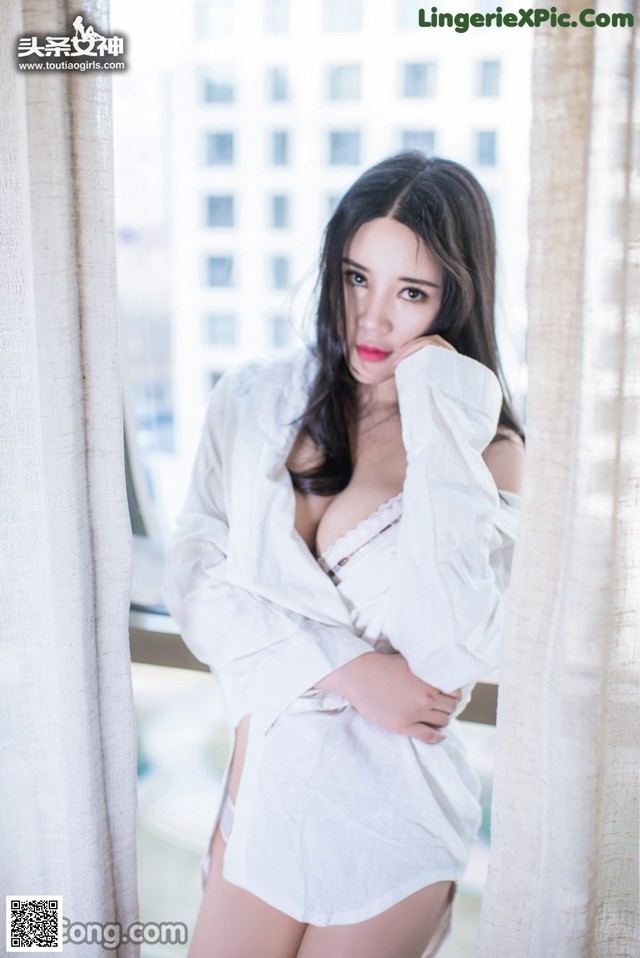 A woman in a white shirt is posing by a window.