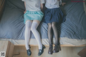 A couple of women sitting on top of a bed.