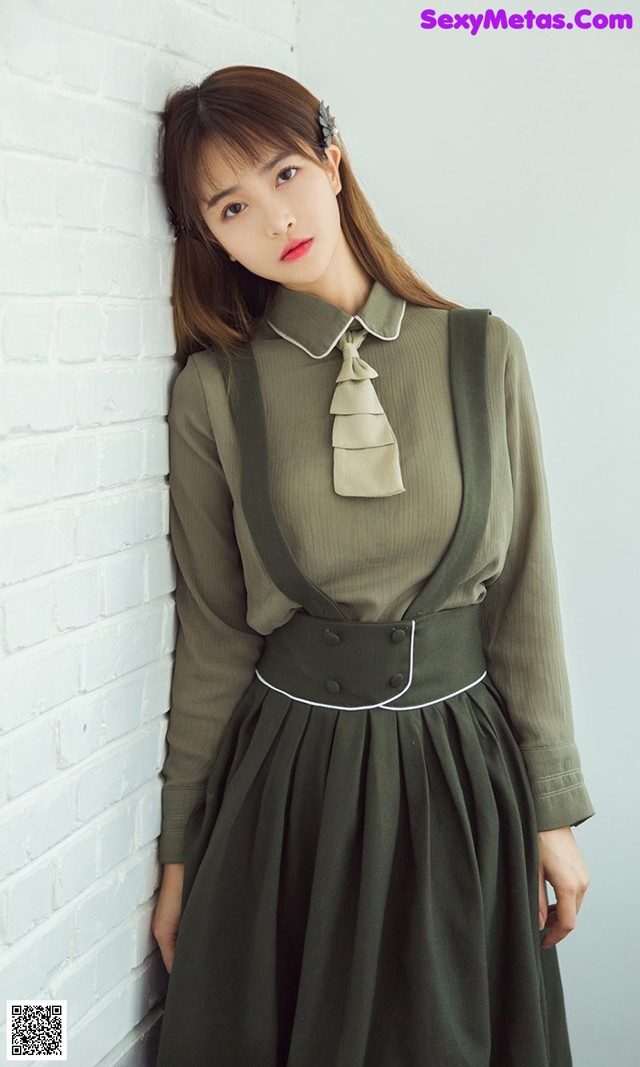 A woman leaning against a white brick wall wearing a green dress.