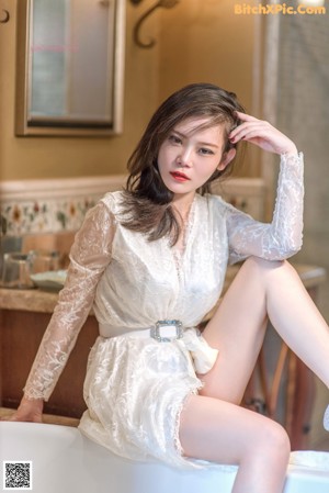 A woman in a white dress sitting on a bed.