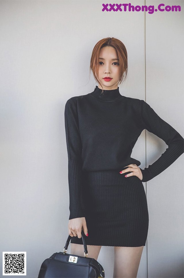 A woman in a black dress holding a black handbag.