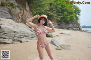 A woman in a bikini and a straw hat posing on a rock.
