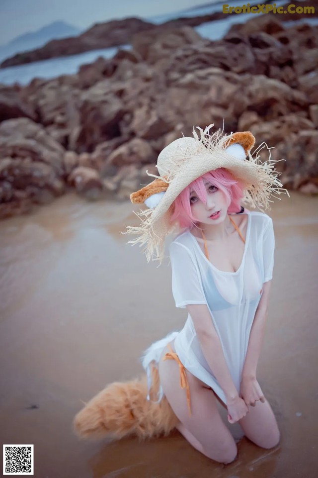 A woman in a white dress and a straw hat on a beach.