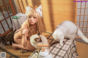 A naked woman sitting on a table next to two cats.