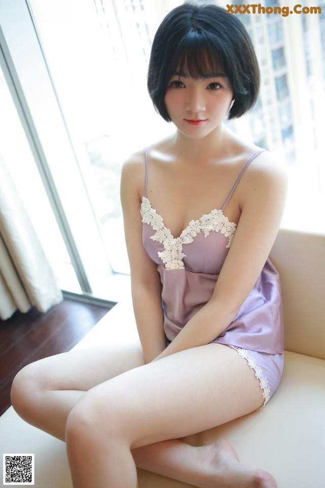 A woman in a purple lingerie sitting on a white couch.