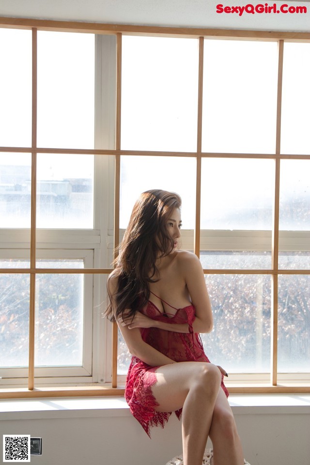 A woman in a red lingerie sitting on a window sill.