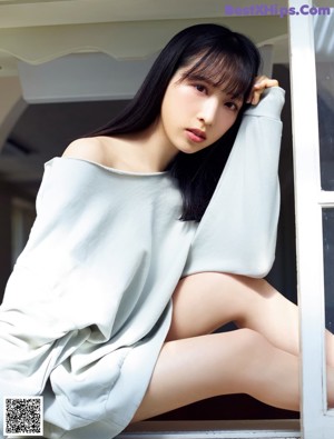 A woman sitting on a window sill in a blue sweater.