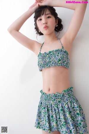 A woman in a bikini top and skirt leaning against a wall.