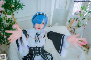 A woman with blue hair sitting on a bed with a teddy bear.