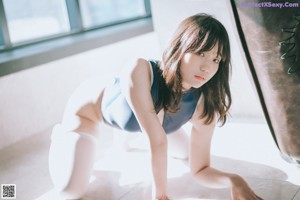 A woman in a blue bodysuit and white stockings is standing by a window.