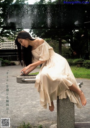 A woman in a black tank top leaning against a wall.