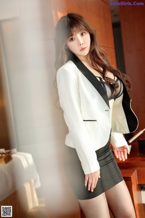 A woman in a white jacket and black skirt posing for a picture.