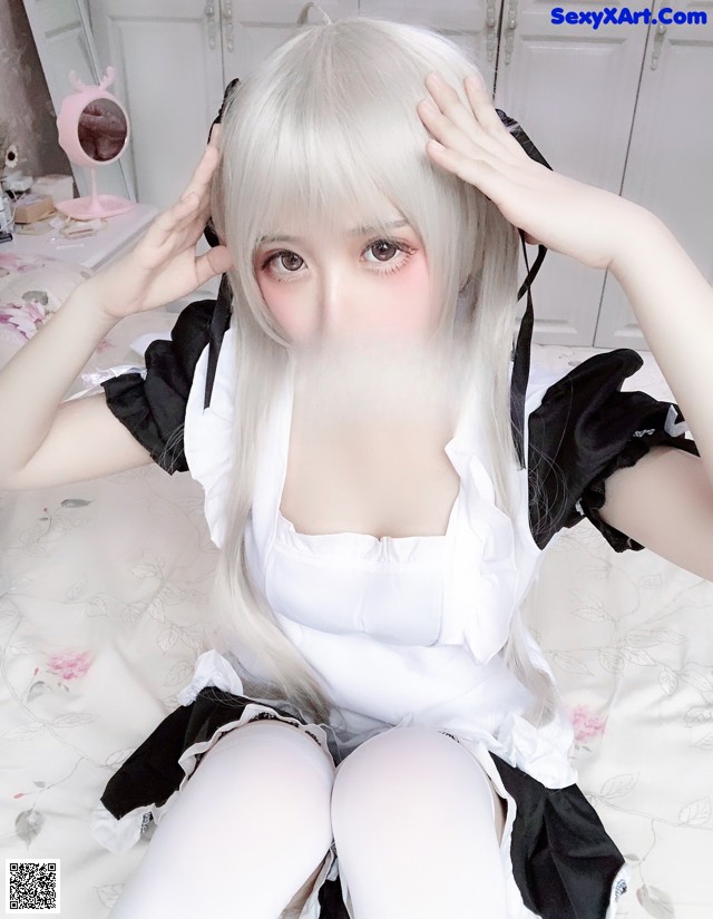 A woman in a maid outfit sitting on a bed.