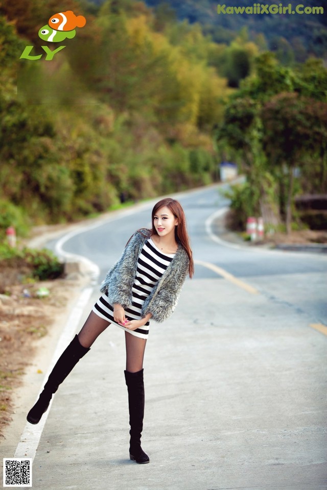 A woman in a striped dress and fur coat posing on a road.