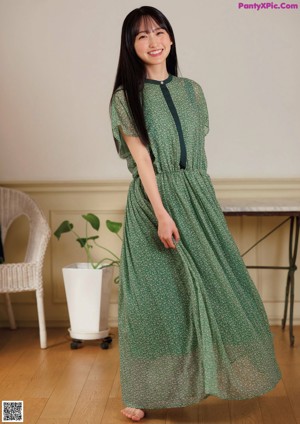 A woman standing in a room wearing a green dress.