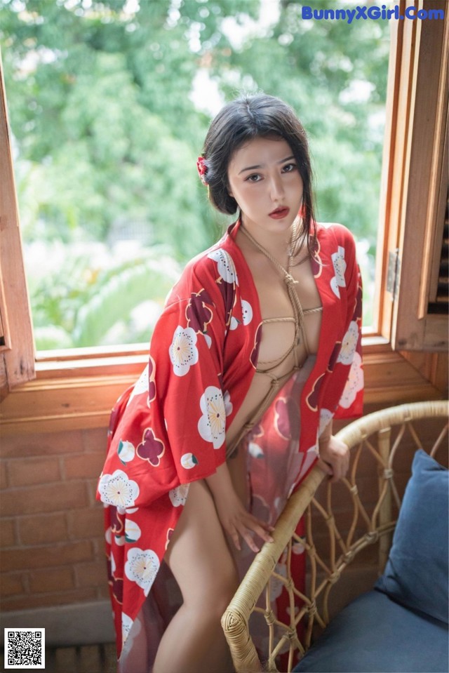 A woman in a red kimono sitting on a chair.