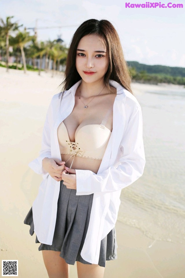 A woman in a white shirt and gray skirt posing on a beach.