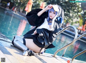 A woman in a black and white outfit sitting by a pool.