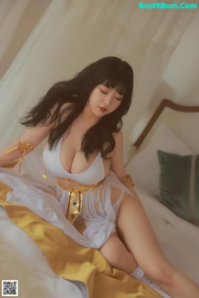 A woman in a white and gold outfit sitting on a bed.