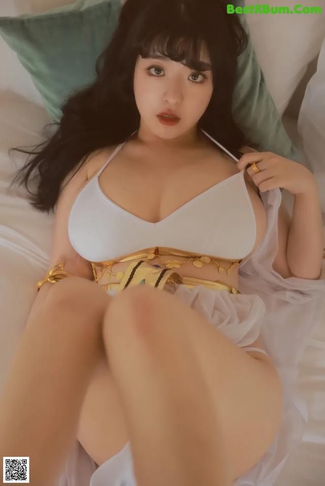 A woman in a white bikini sitting on a bed.