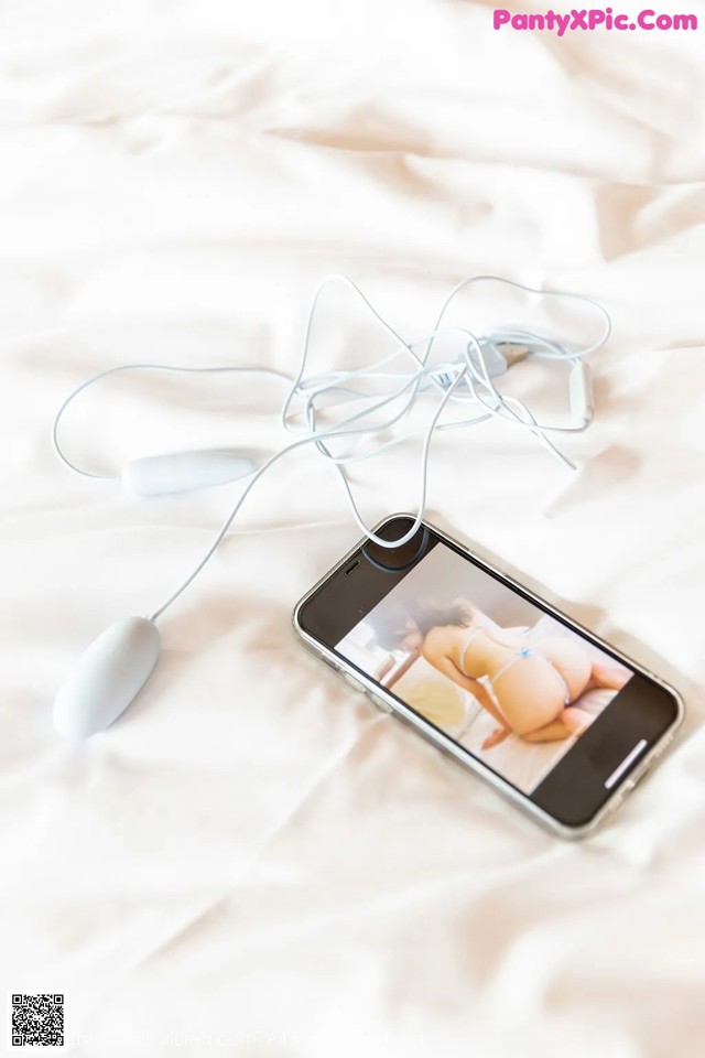 A cell phone sitting on top of a bed next to a pair of earphones.